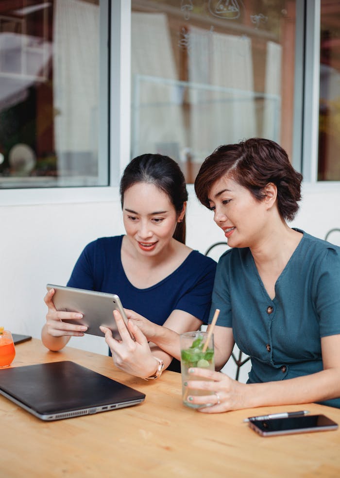 Two women enjoy browsing on a tablet together in an outdoor café.